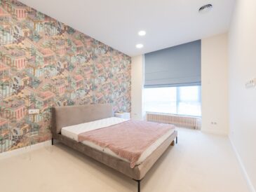 Interior of light apartment with bed near colorful wall and jalousie on window in daylight