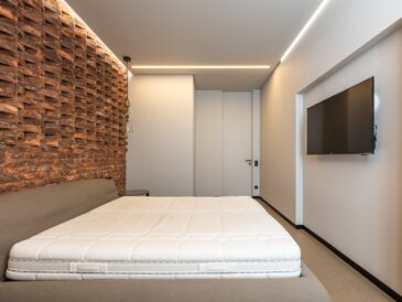 Comfortable be with soft mattress in stylish minimalist bedroom with modern TV and creative brick wall