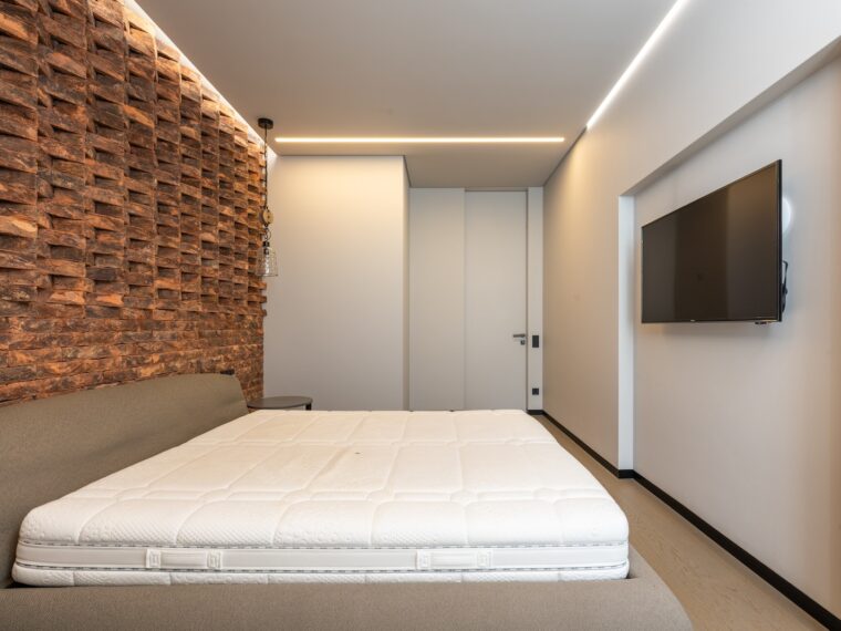 Comfortable be with soft mattress in stylish minimalist bedroom with modern TV and creative brick wall