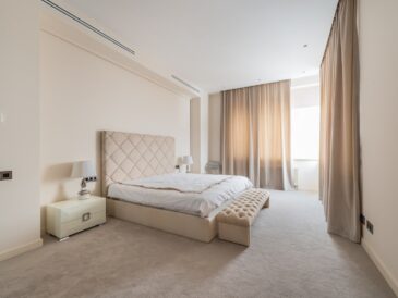 Soft ottoman bench placed near comfortable bed in spacious minimalist bedroom decorated with beige curtains in daylight